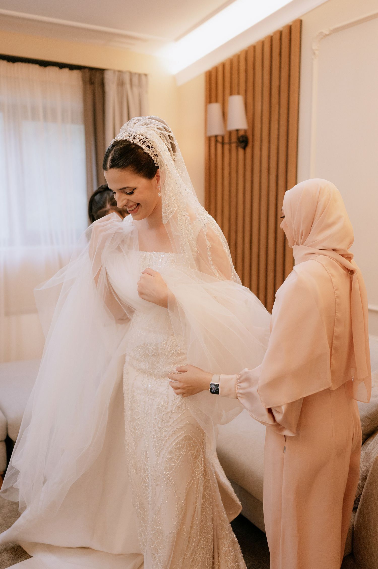 Wedding preparations show helpers adjusting a flowing white veil on an elegant bridal gown.