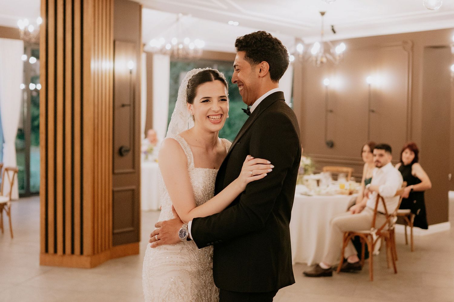 Wedding reception dance in an elegant ballroom with wooden accent walls and chandeliers.