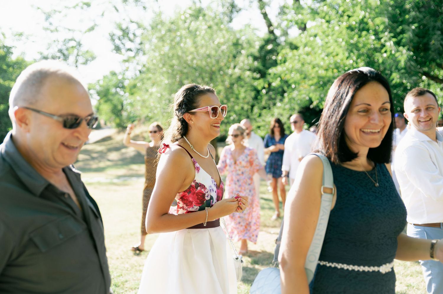 Wedding party gathers for candid moments during an outdoor celebration in a lush green setting.