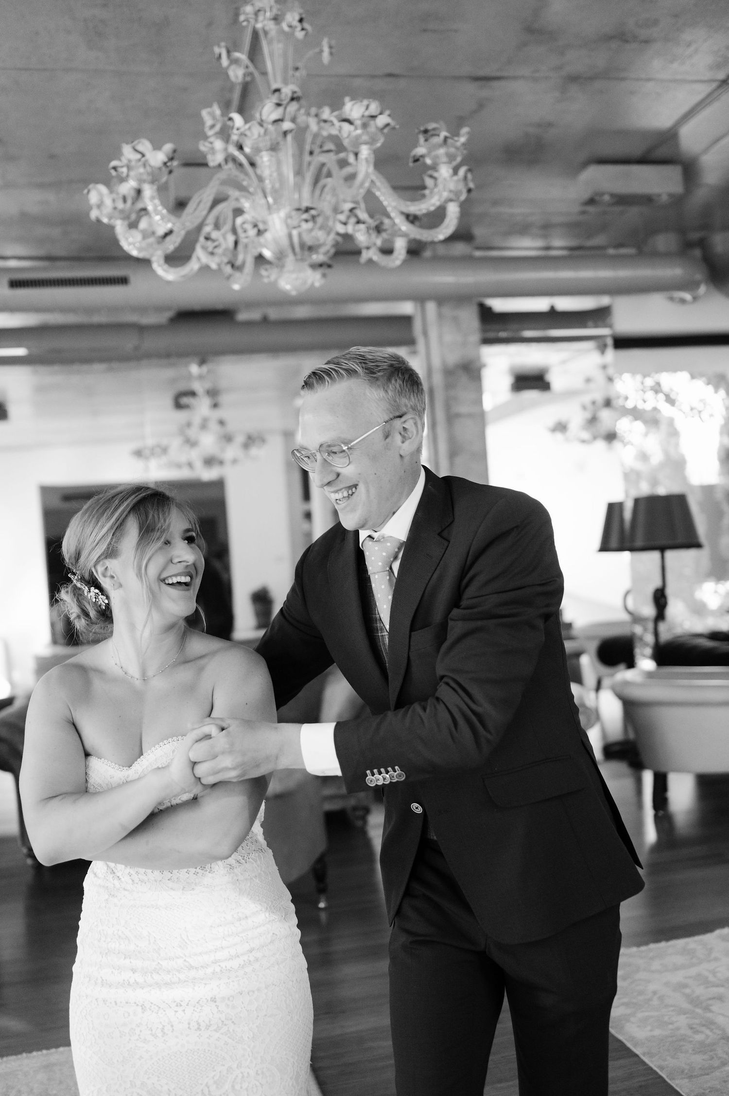 A black and white photo captures a candid moment of laughter between a couple on their wedding day.