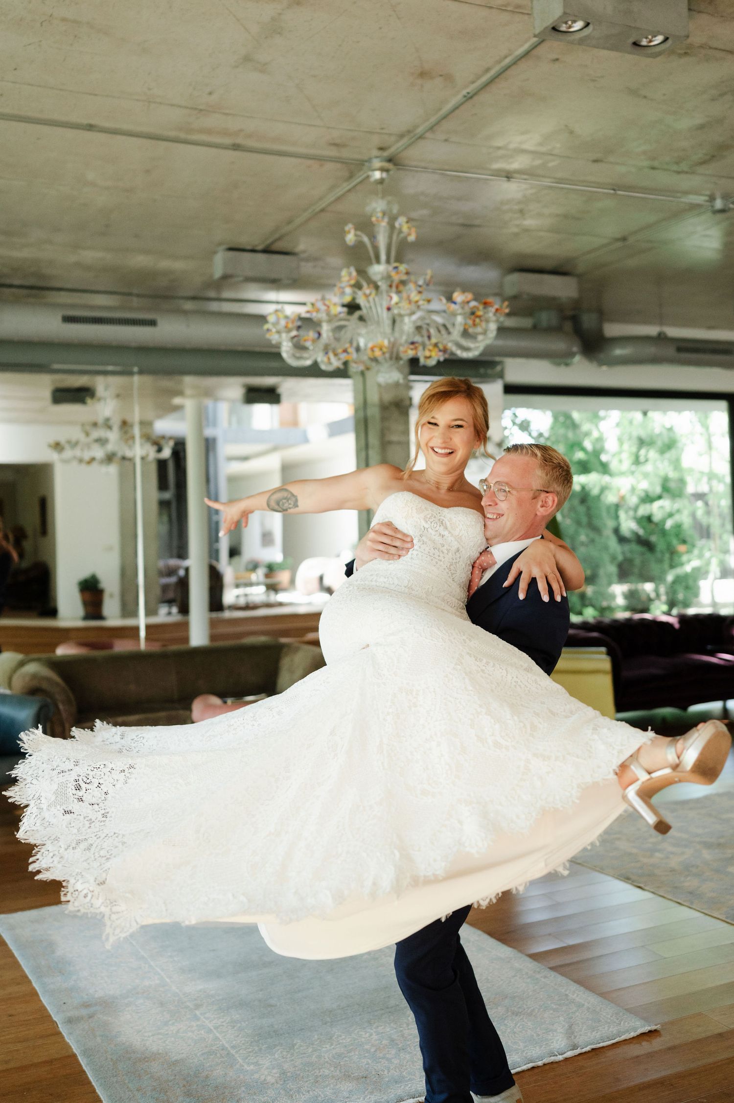 Joyful wedding couple performing dramatic dance lift in reception hall.