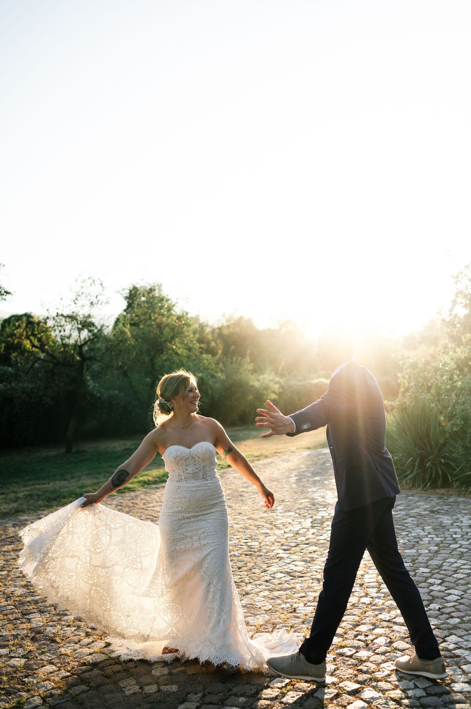 Romantic wedding couple dancing on cobblestone path during golden sunset.