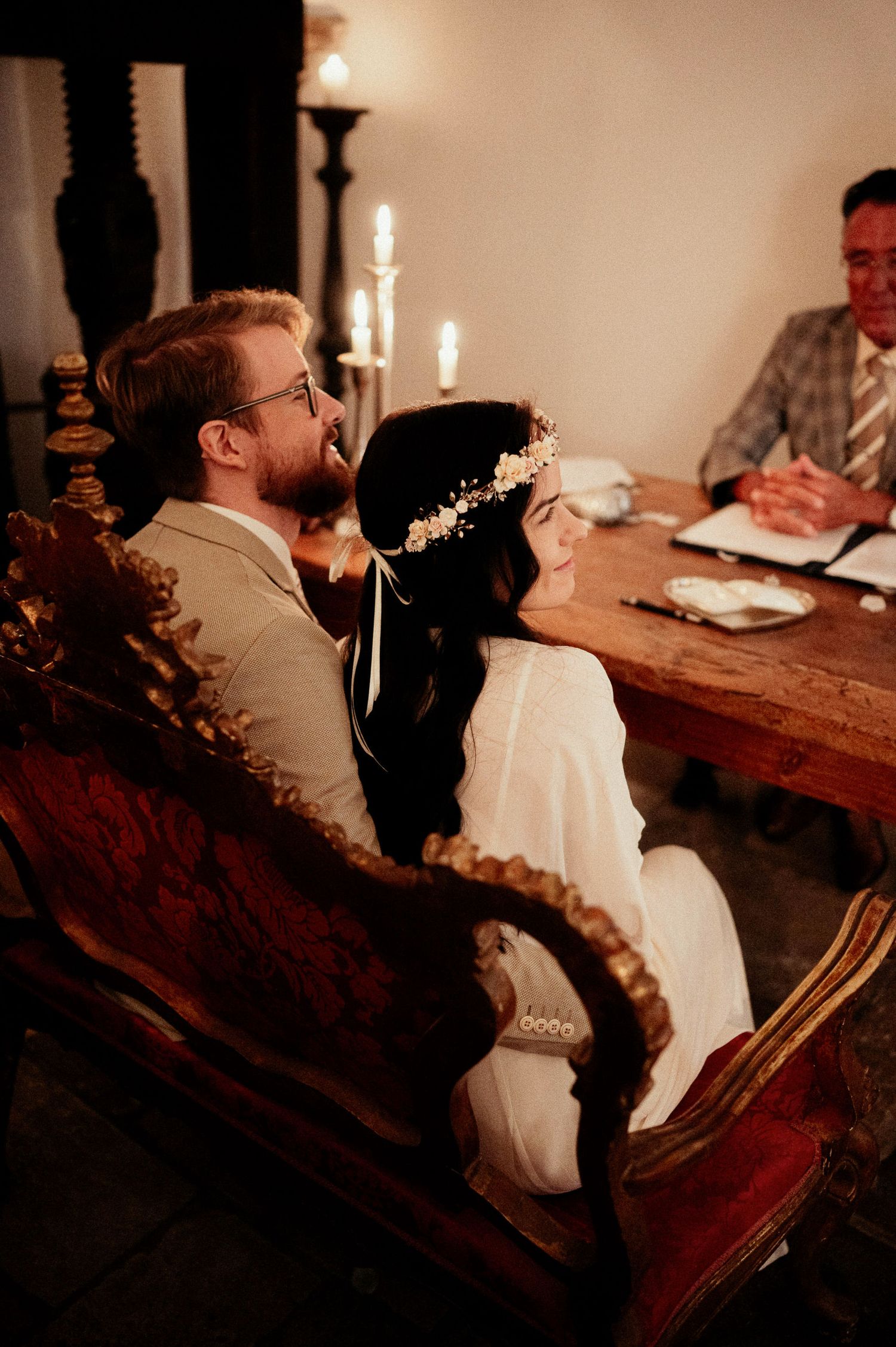 Couple seated at wooden table during intimate ceremony with candlelight.