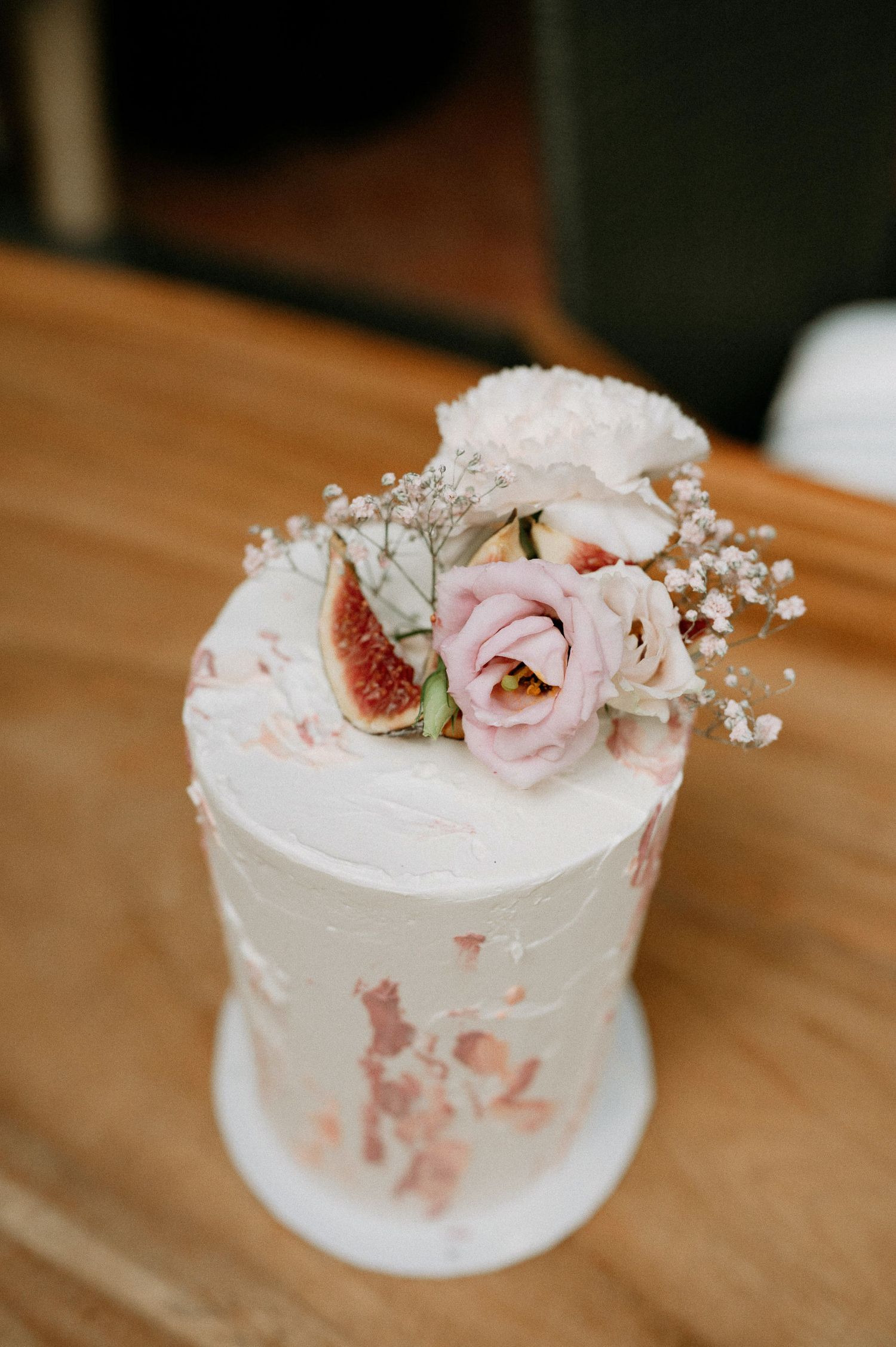 Small white wedding cake decorated with delicate pink roses and figs on a wooden table.