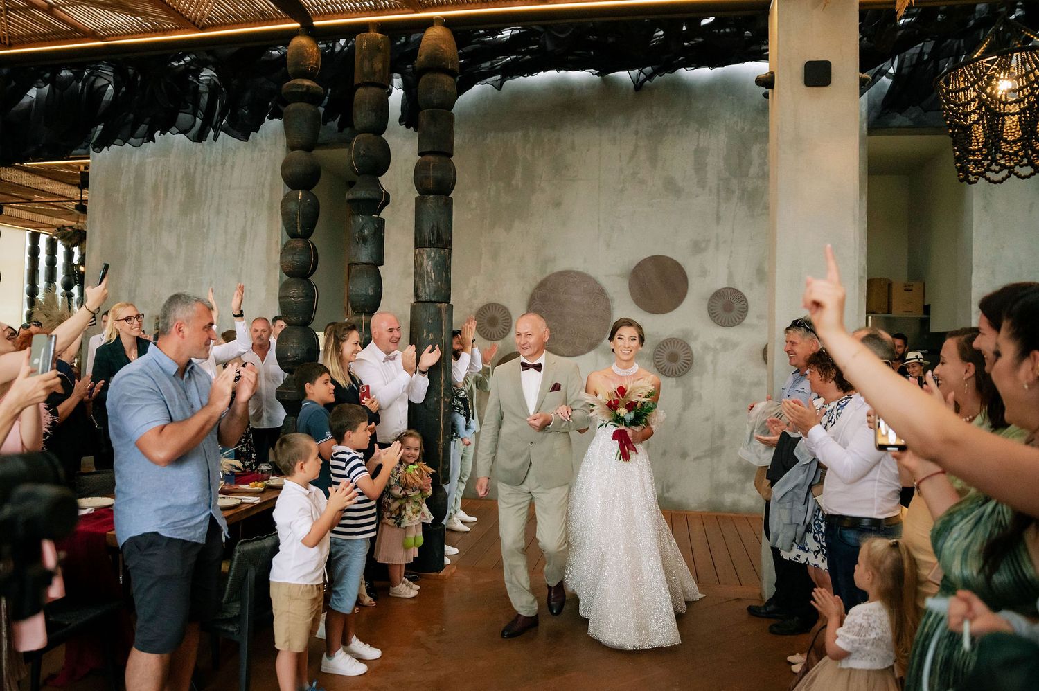 Wedding guests cheer and applaud during an emotional reception moment in an industrial-style venue.