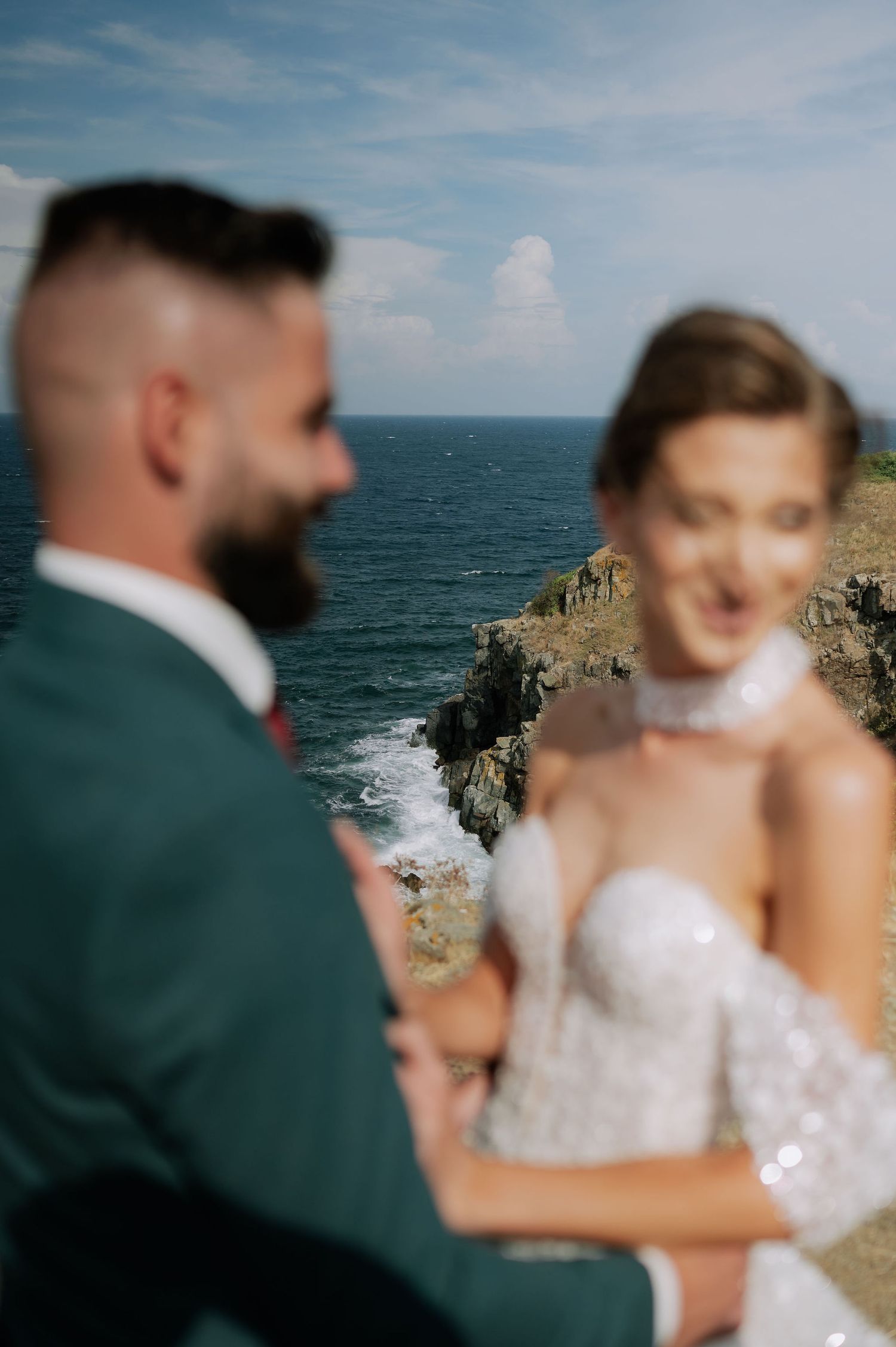 An intimate wedding moment captured against a backdrop of ocean cliffs and blue skies.