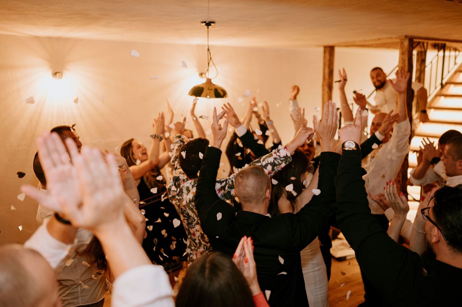 Sepia-toned image of wedding party guests dancing and celebrating with hands in the air.
