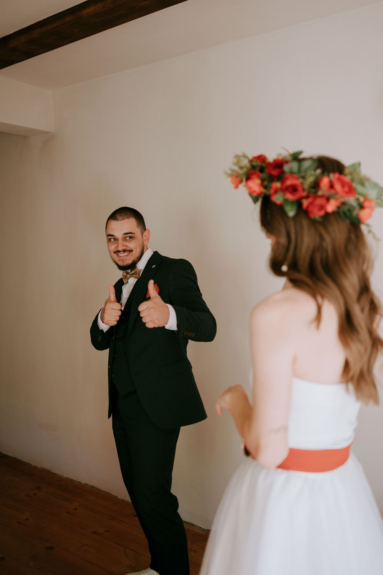 A playful first look moment between a couple on their wedding day, with the groom in black suit reacting joyfully.