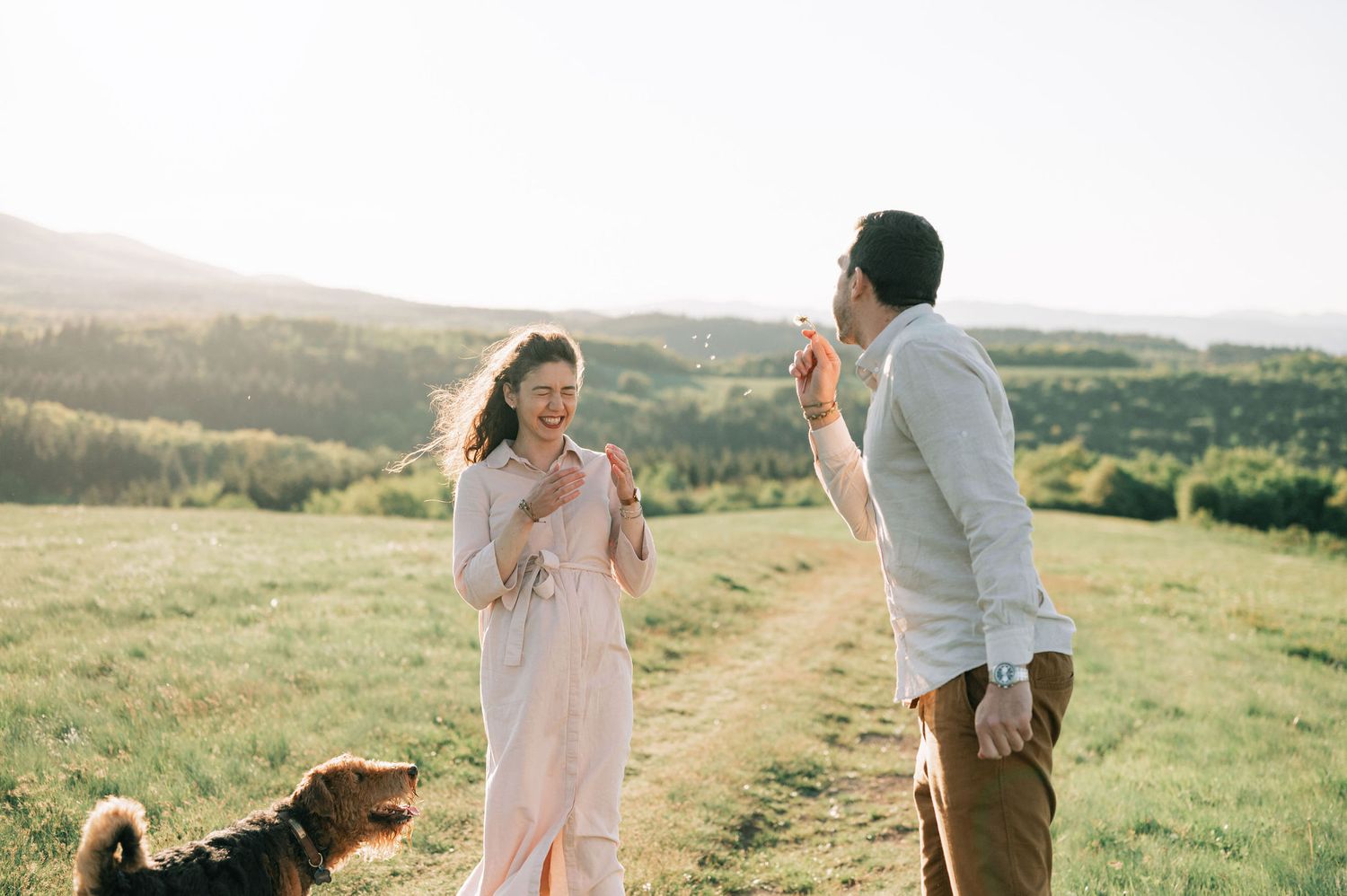A couple walks together through a scenic green meadow during golden hour at sunset.