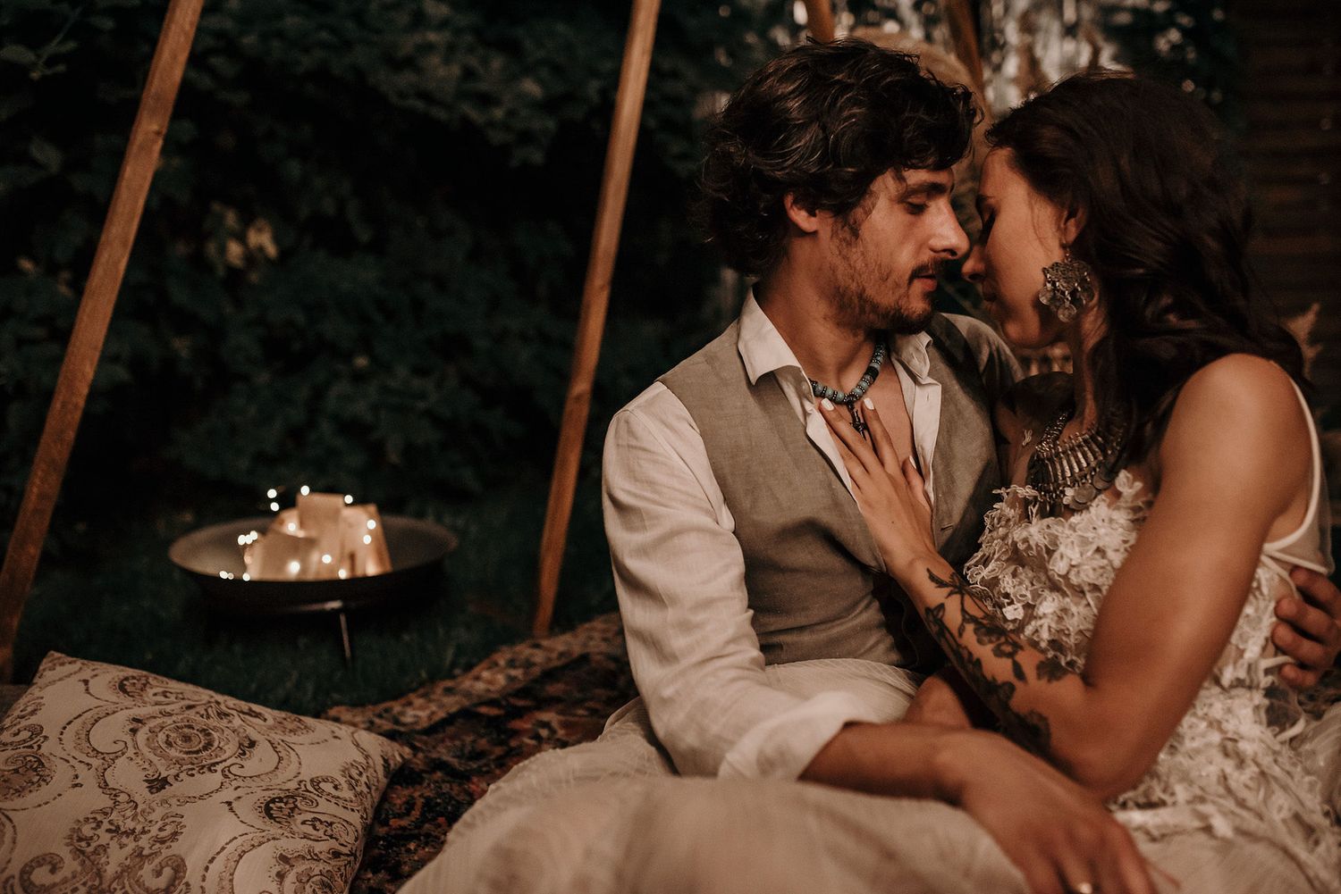 A romantic couple shares an intimate moment in a dimly lit outdoor setting with string lights overhead.
