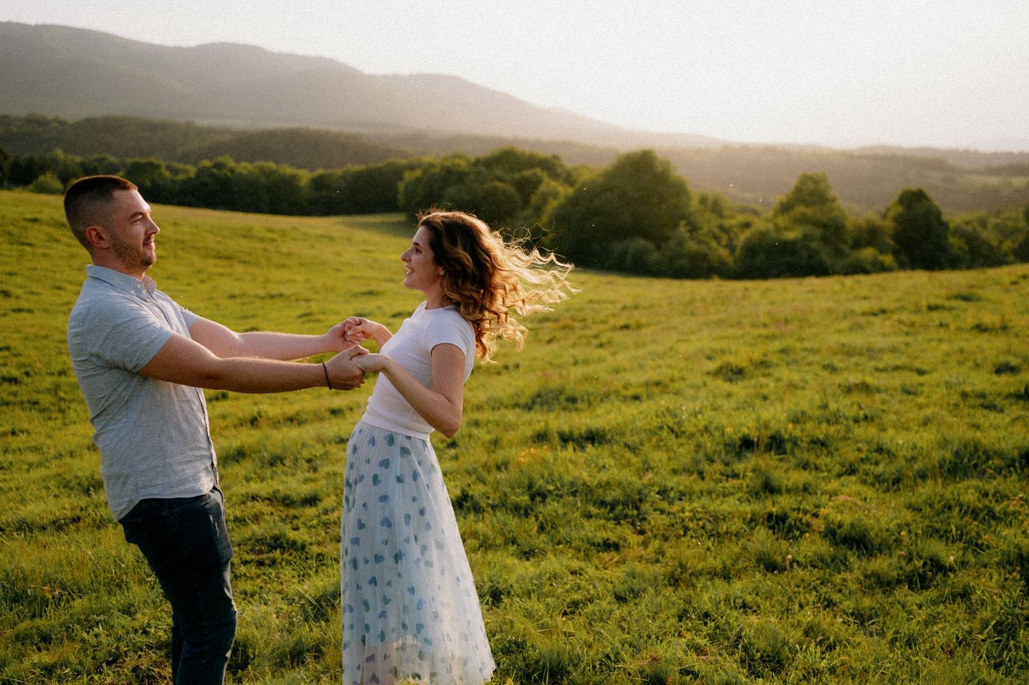 Dancing couple spinning in a grassy meadow during sunset with mountains in view.