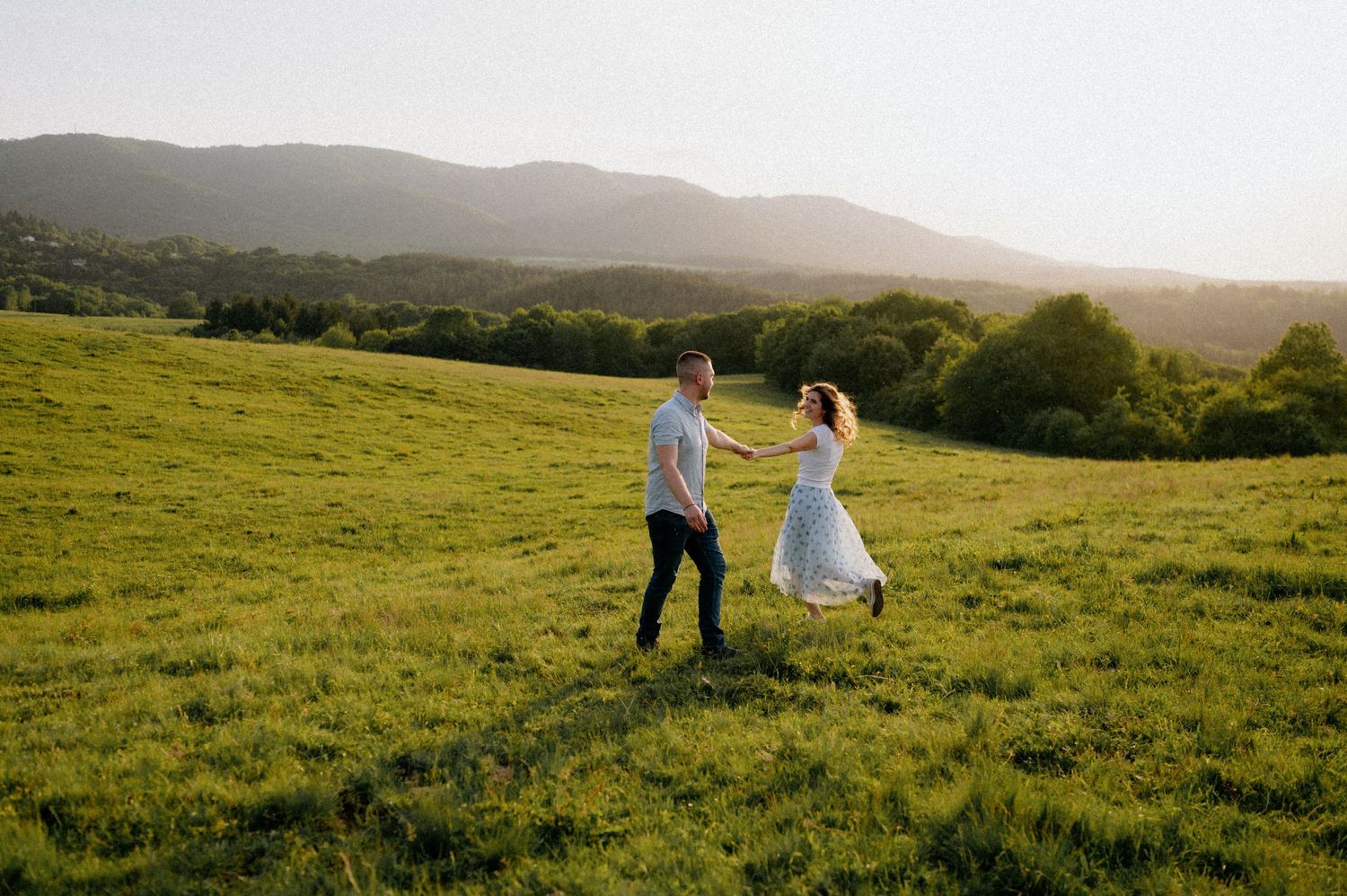 Two people share a tender moment while dancing in a sunlit mountain meadow.