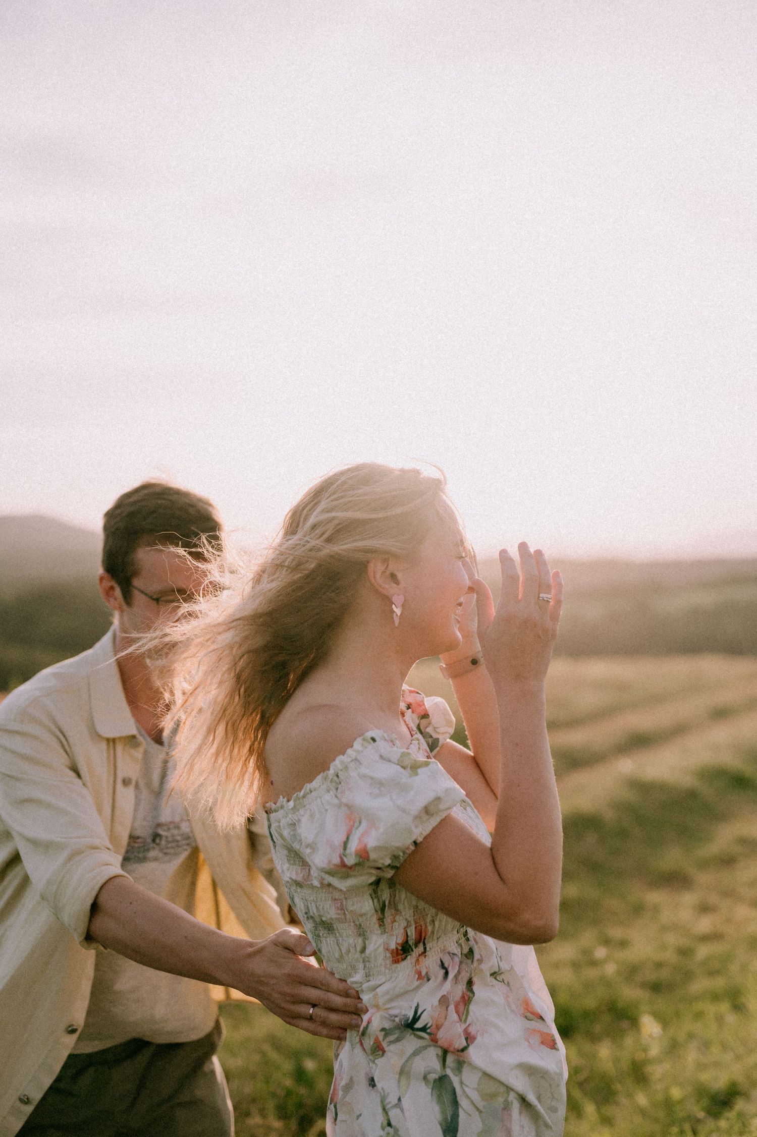 A romantic couple shares a playful moment in a sunlit meadow at golden hour.