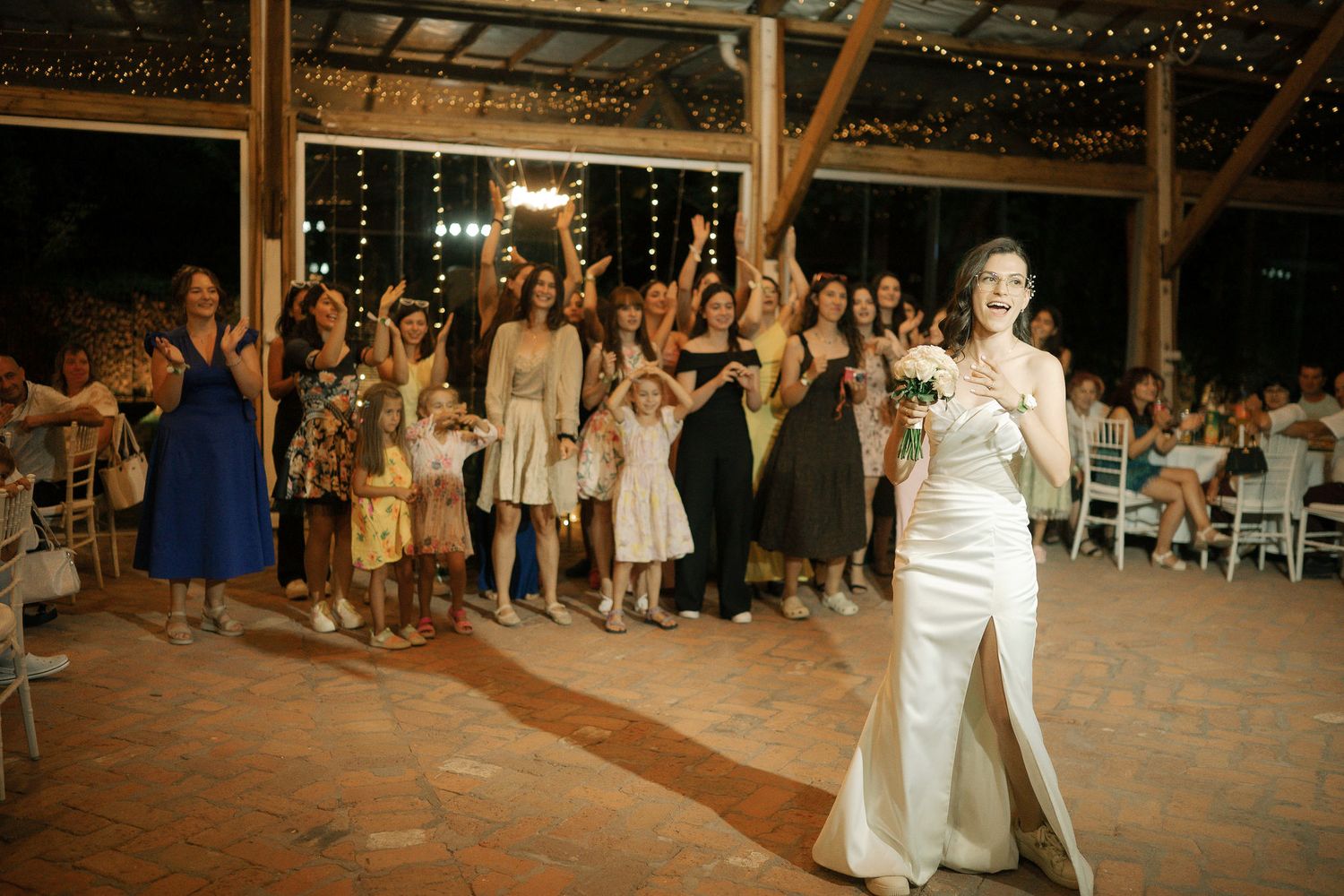 Wedding guests dance and celebrate on a rustic wooden dance floor under twinkling string lights.