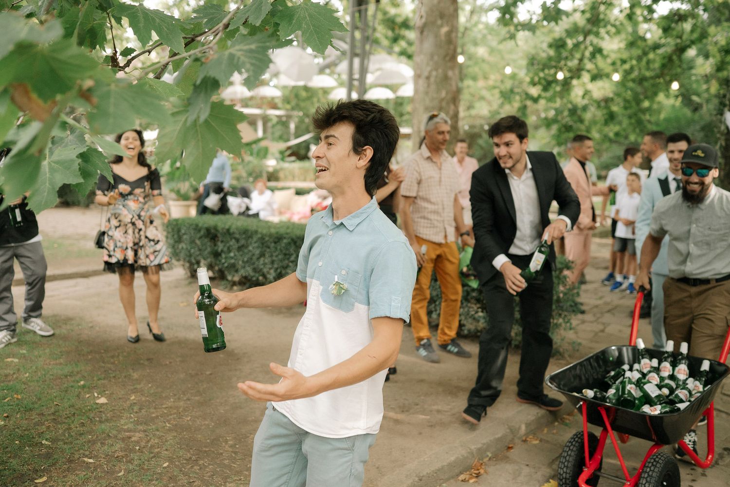 A group of people dance and celebrate at an outdoor wedding reception under green trees in a garden setting.