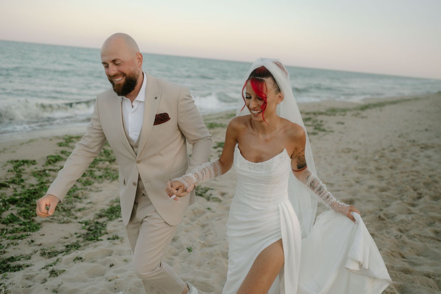 A romantic beach wedding photoshoot with couple walking along the shore at sunset in elegant attire.