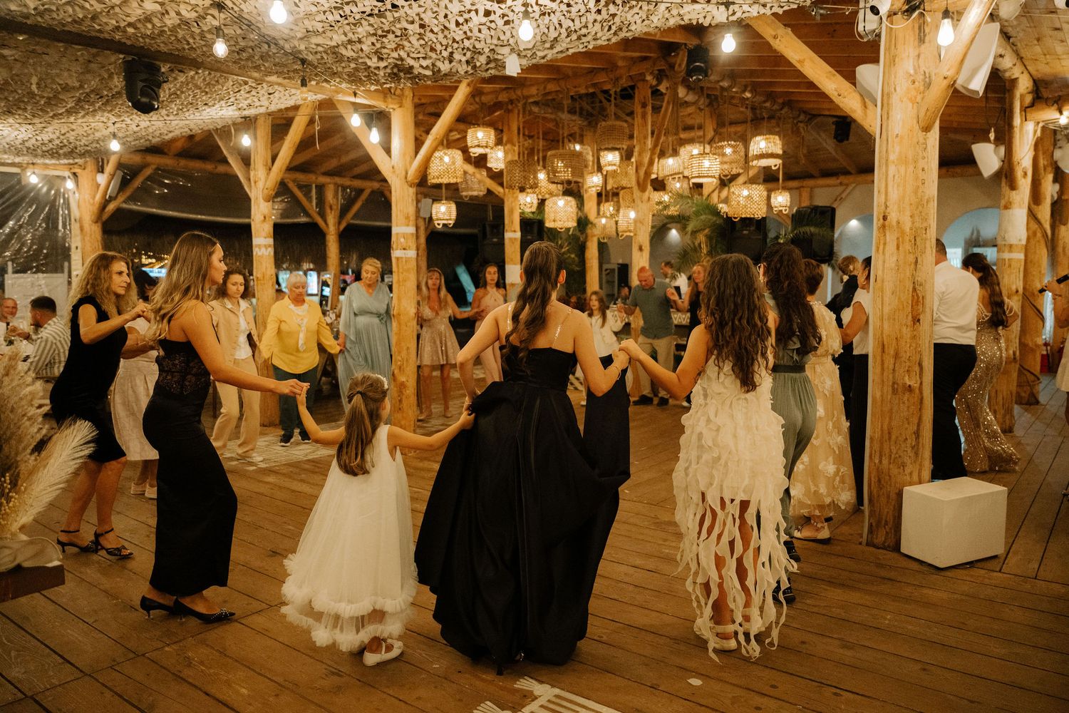 People dancing at a rustic barn wedding reception with wooden beams and twinkling lights overhead.