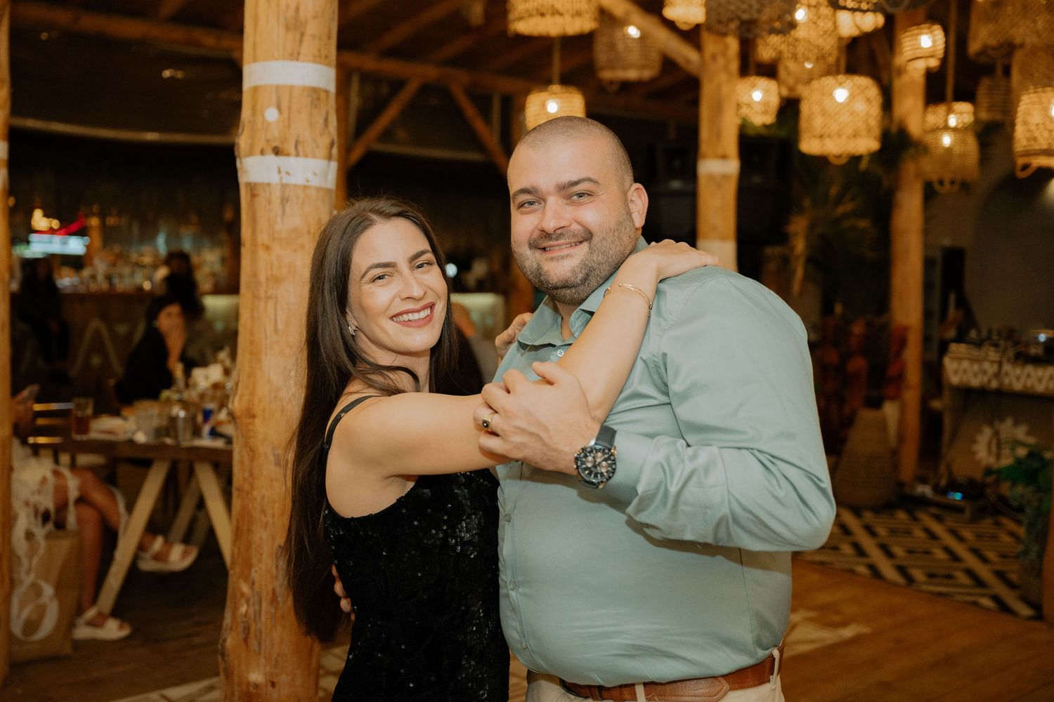 People dance together at a nighttime outdoor venue with wooden posts and string lights creating a festive atmosphere.