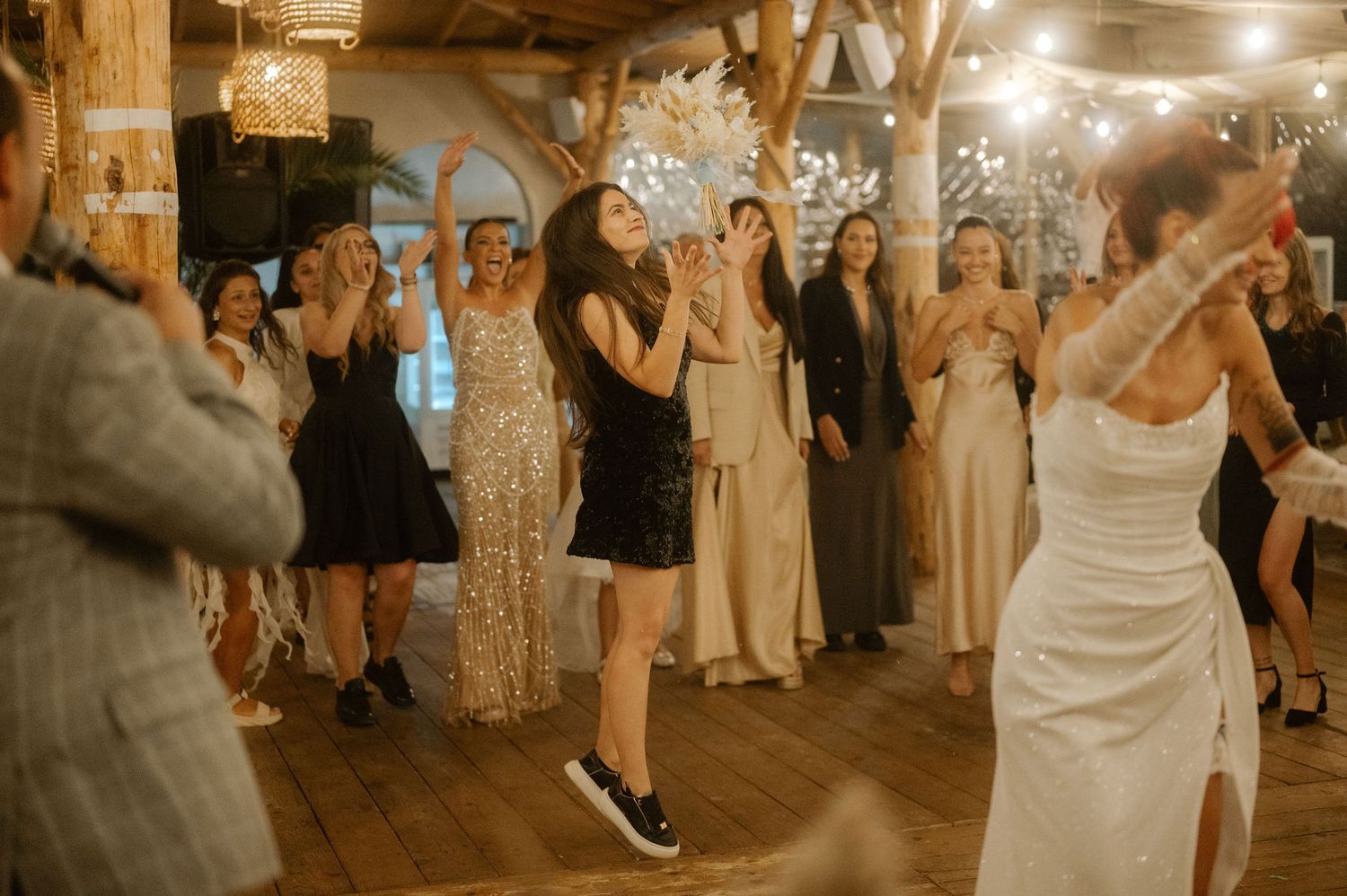 Wedding guests dance and celebrate on a rustic wooden dance floor during an evening reception.