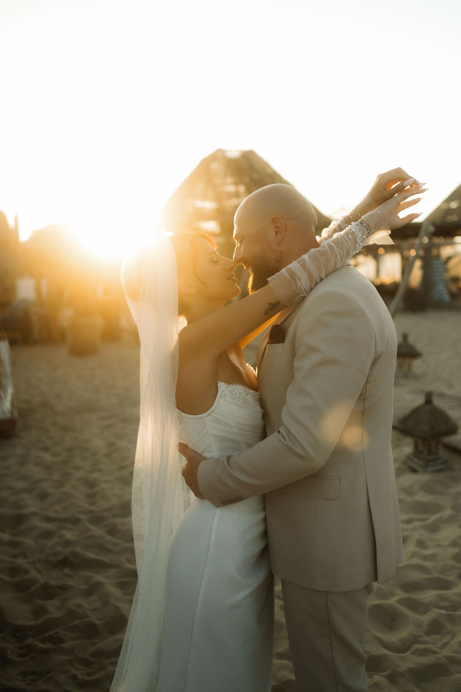A couple shares a romantic kiss on the beach during golden hour with sunlight creating a dreamy silhouette.