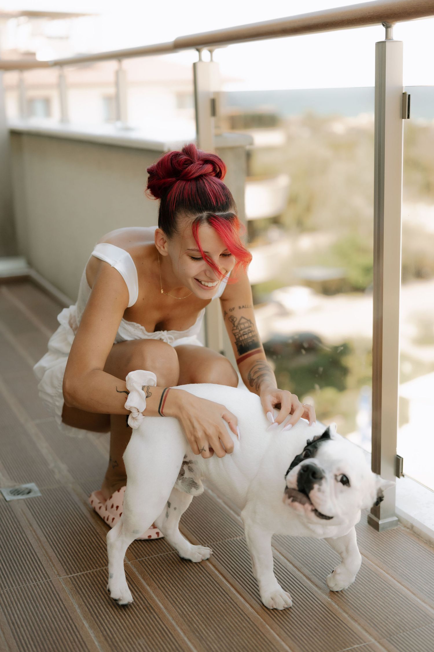Person with red hair plays with two white cats on a balcony while enjoying a sunny afternoon.