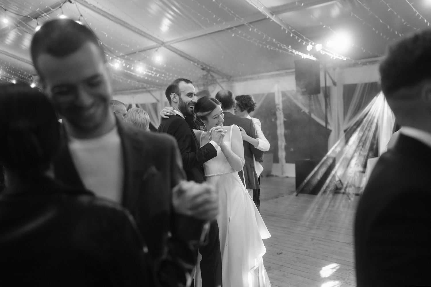 Black and white photo of couples dancing at a wedding reception under indoor lighting.