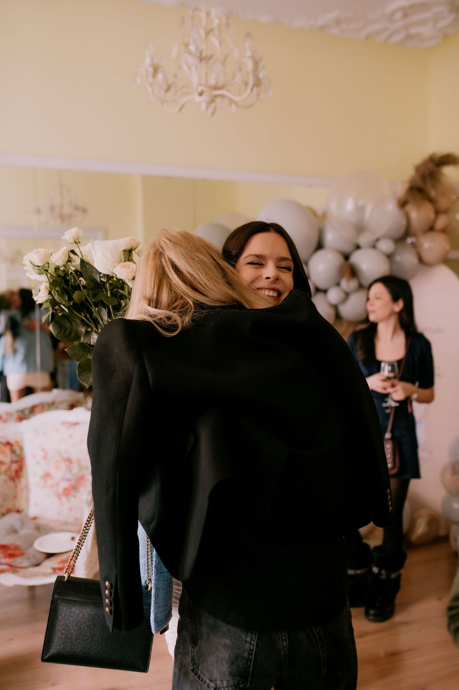 A group of people in black attire embracing and hugging at an indoor event with white balloons in the background.