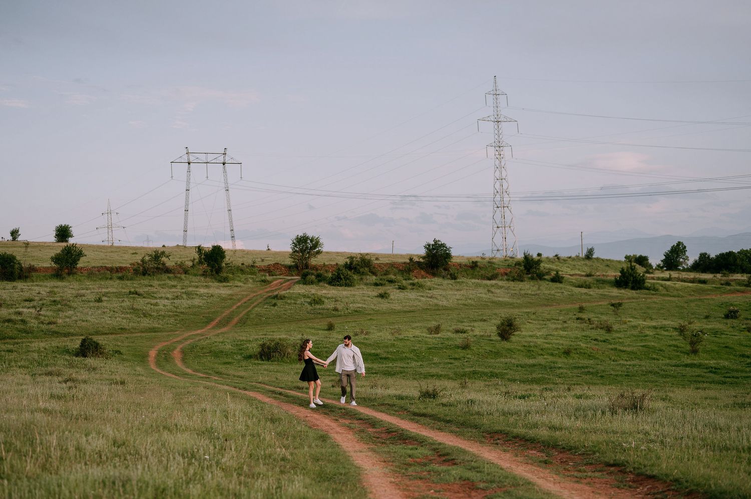 Dirt paths wind through grassy plains with power lines and transmission towers stretching across the horizon.