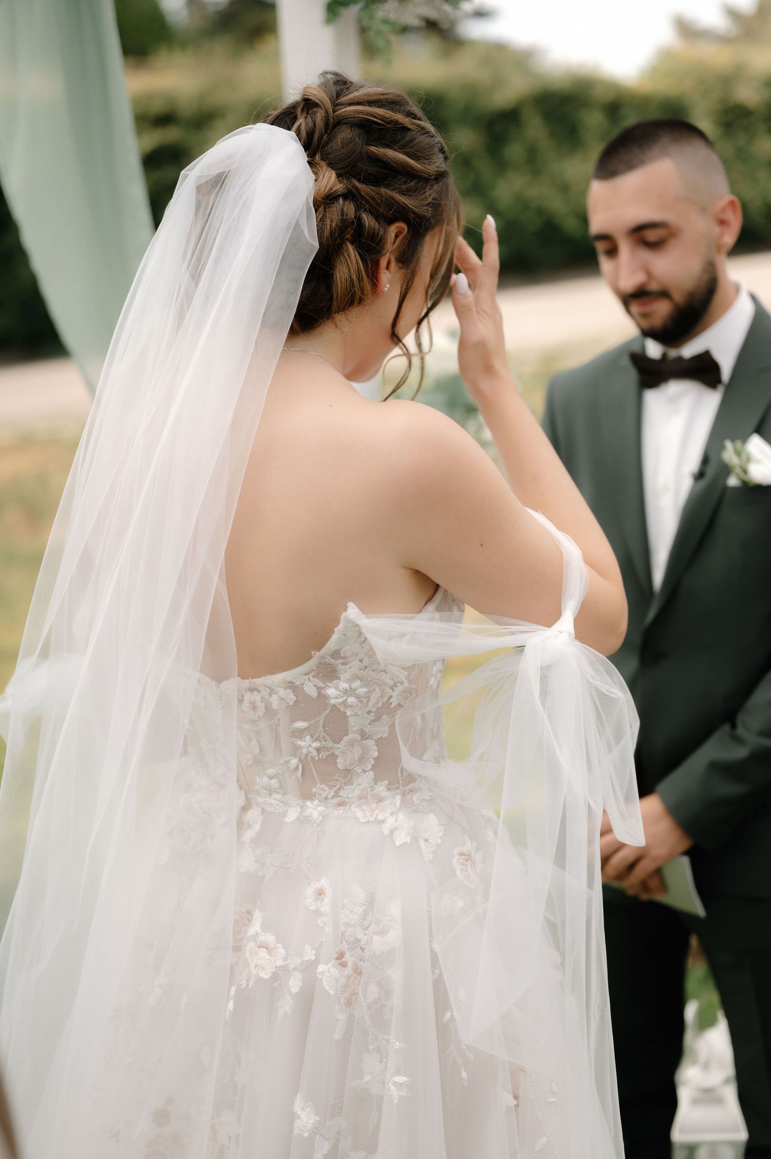 An elegant wedding dress with delicate lace details and flowing veil captured during an outdoor ceremony.