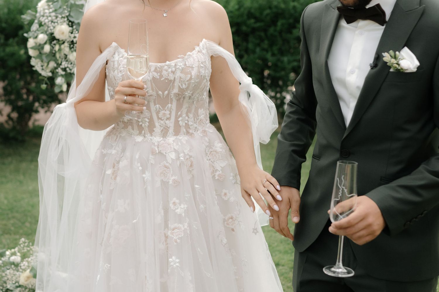 A couple in formal wedding attire clinks champagne glasses during an elegant outdoor celebration.