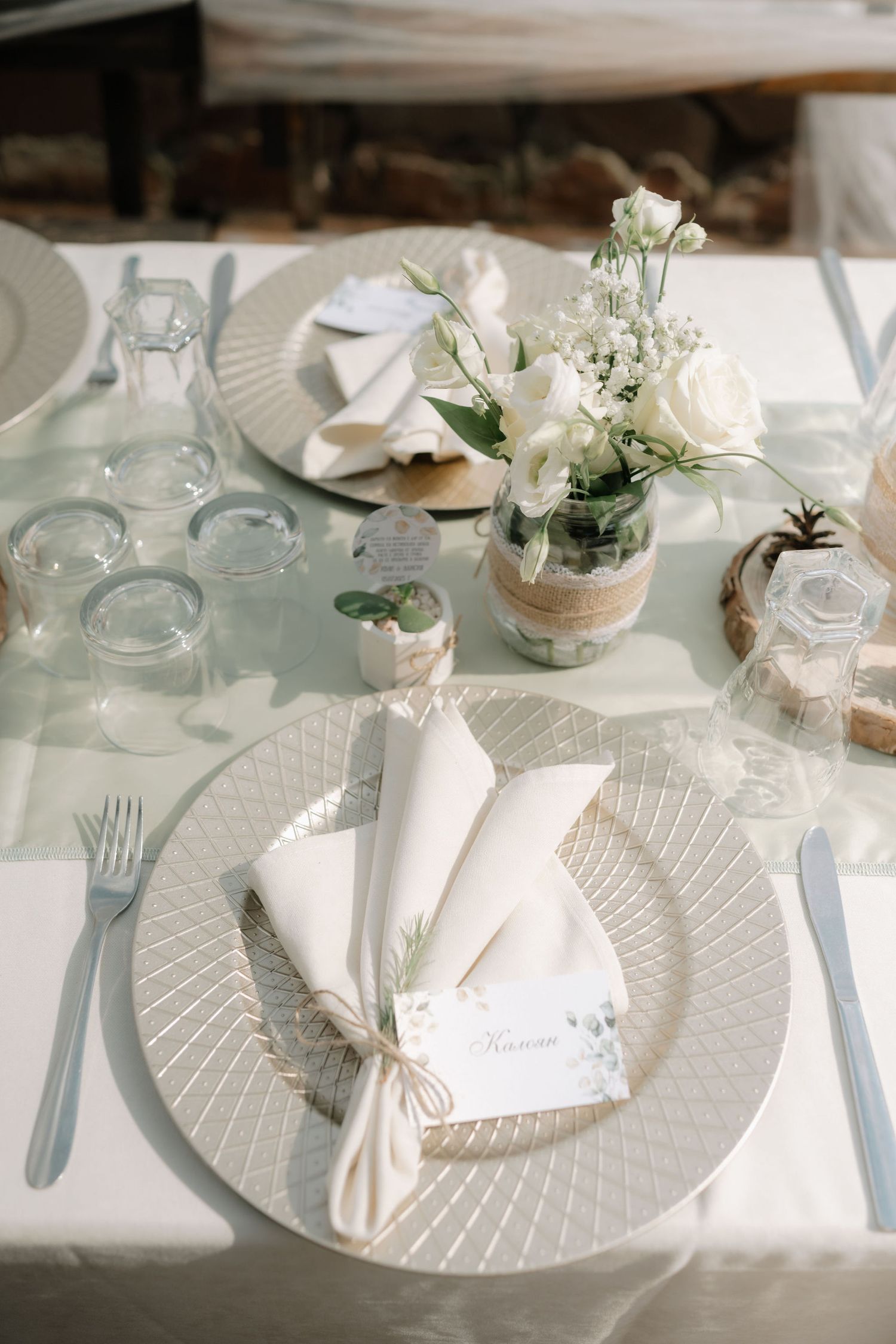 White and beige table settings with textured plates, glass jars, and delicate floral accents at an outdoor venue.