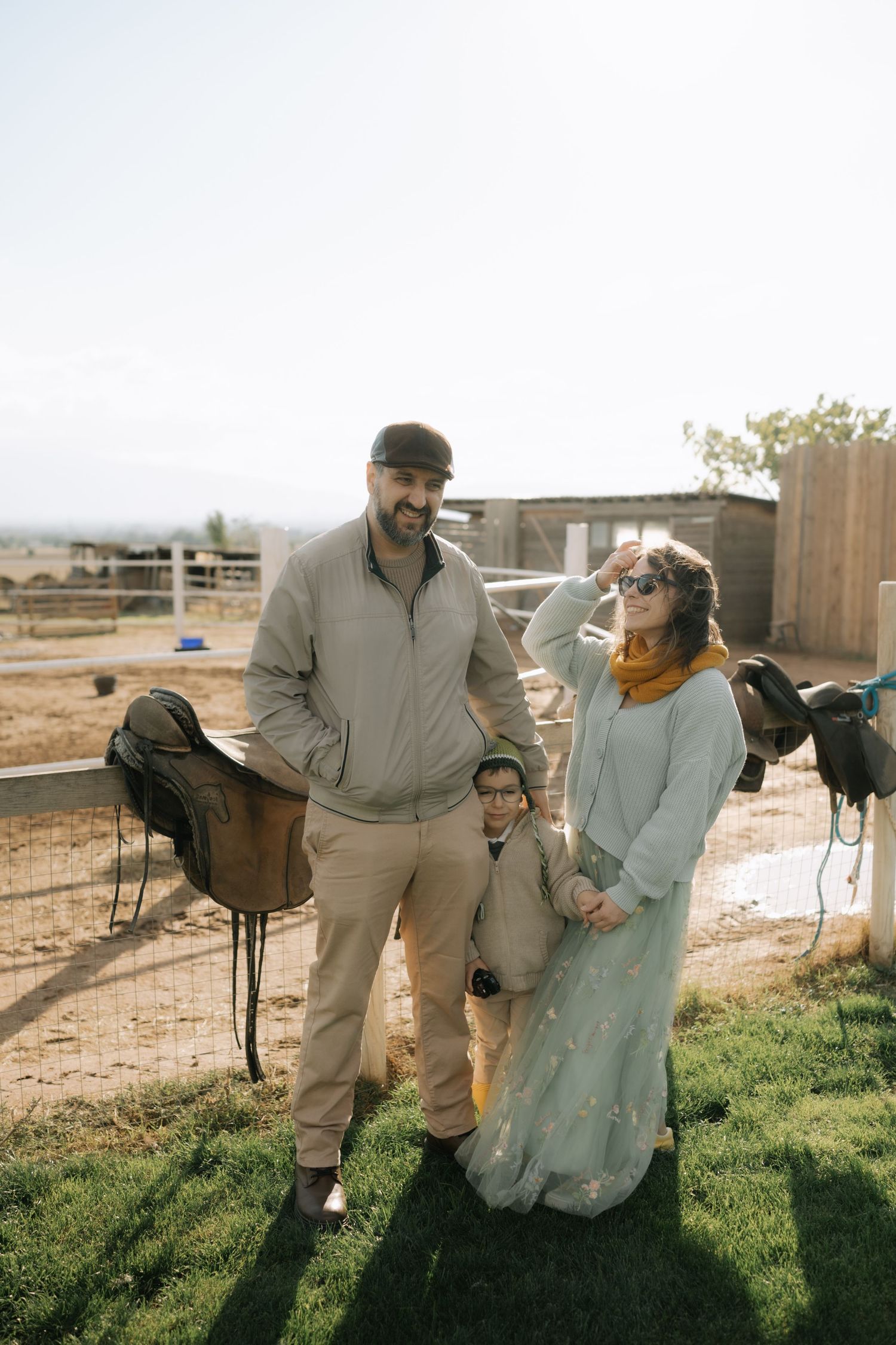 A couple in wedding attire playfully interacts in a rustic outdoor setting with horses visible in the background.