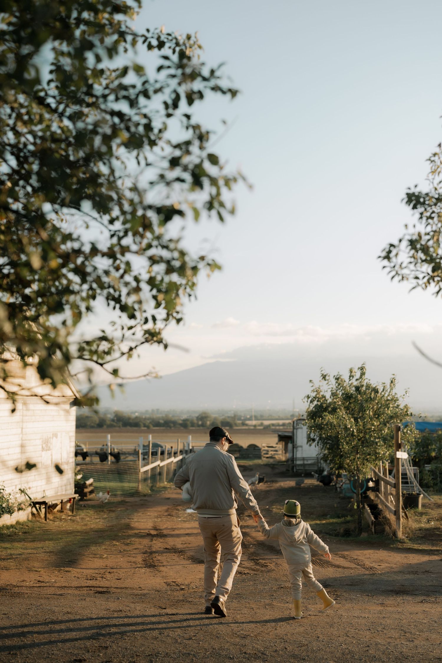 Two people play together at sunset on a dirt path with trees and mountains in the background.