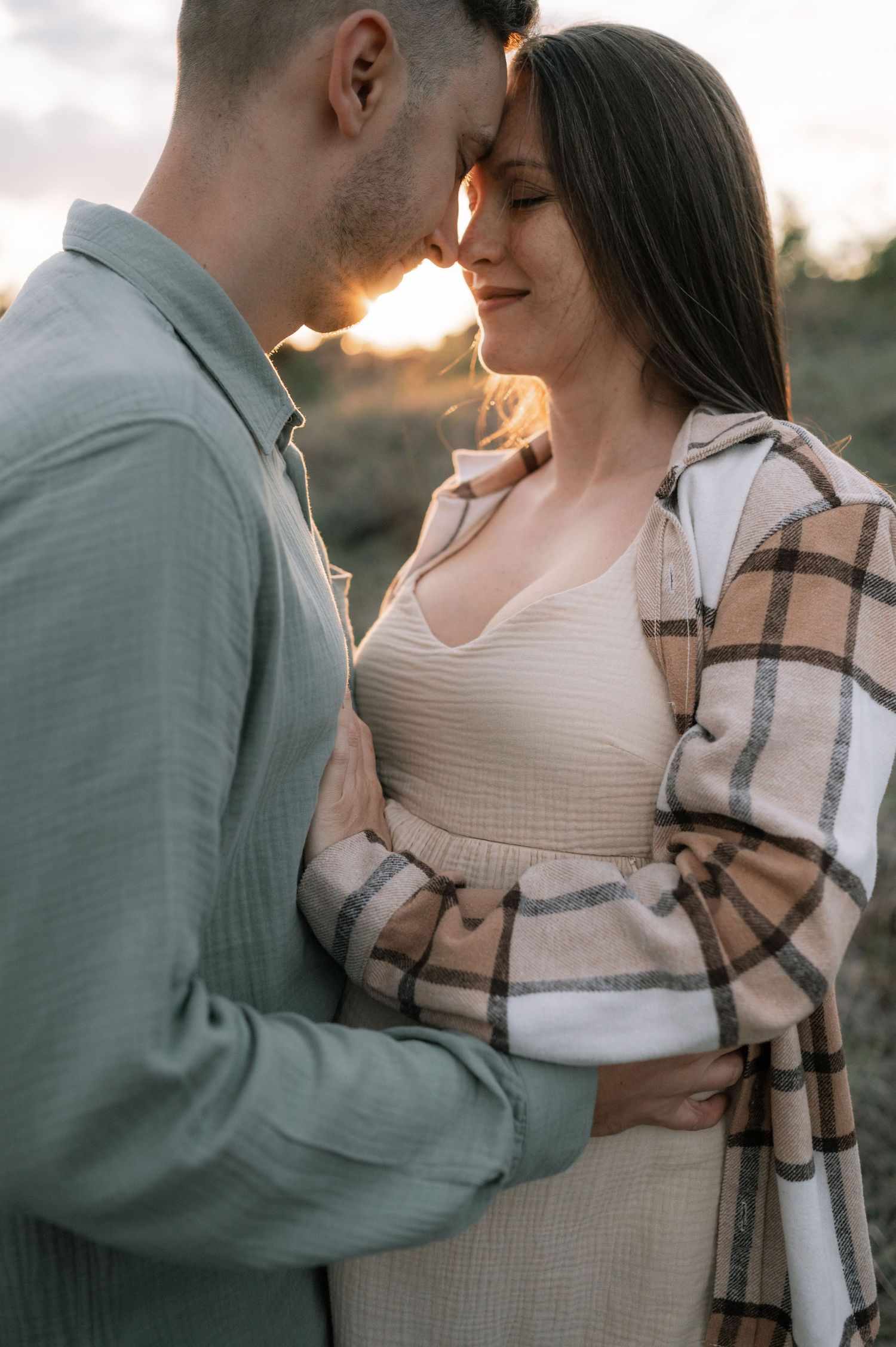 Intimate maternity photo session at sunset showing a couple embracing in soft natural light.