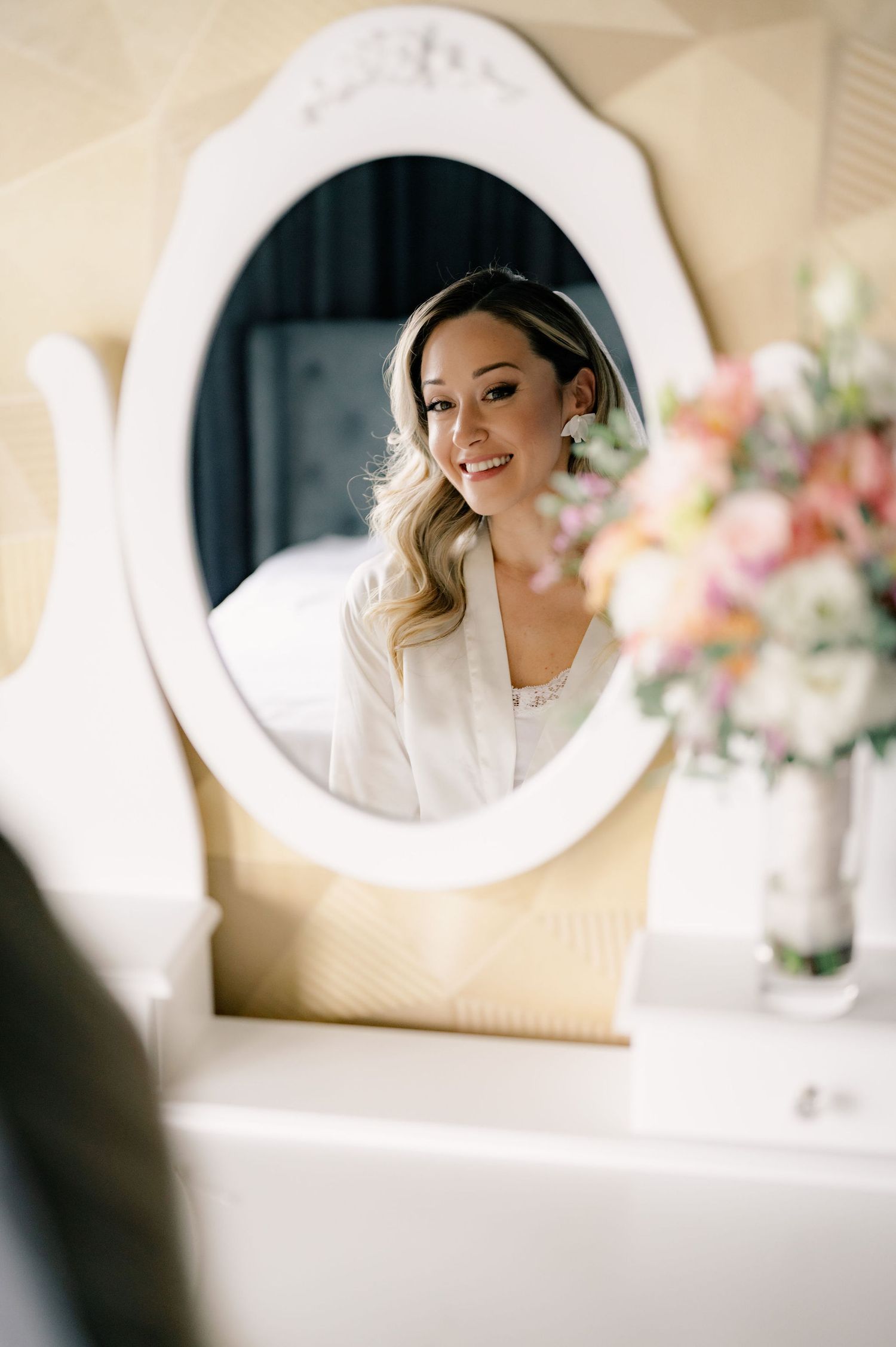 A series of circular mirrors reflect a bride getting ready on her wedding day with soft romantic lighting and floral decor.