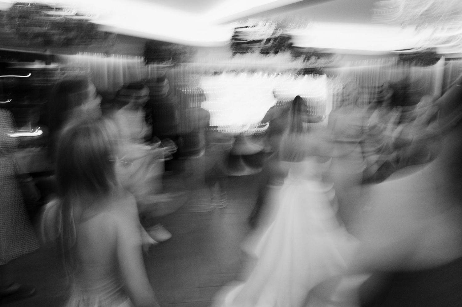 Black and white motion blur photograph of people dancing at an event shows abstract movement and energy.