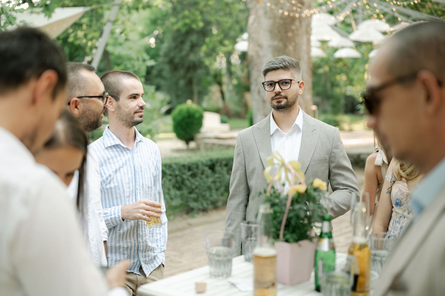 Group of people enjoying drinks and conversation at an outdoor garden party on a sunny afternoon.