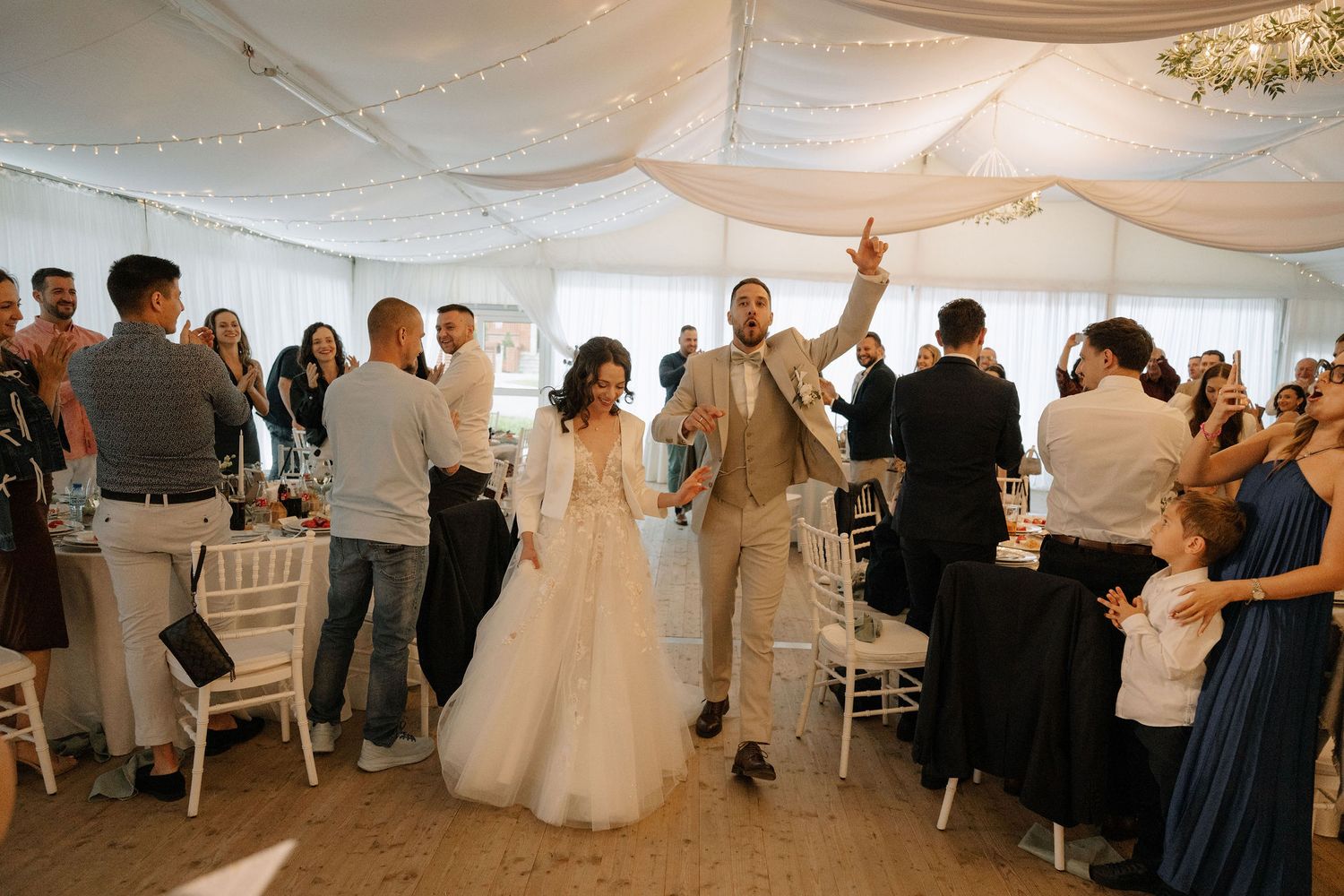 Bride and groom make grand entrance at elegant wedding reception as guests cheer and celebrate.