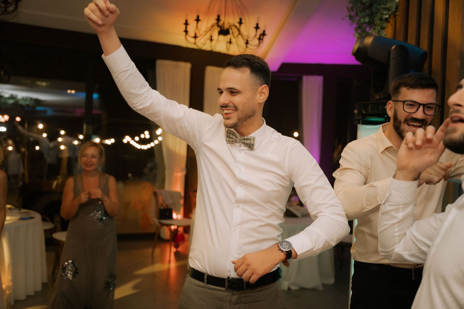 Wedding guests dance and celebrate with raised arms on an illuminated dance floor at an evening reception.