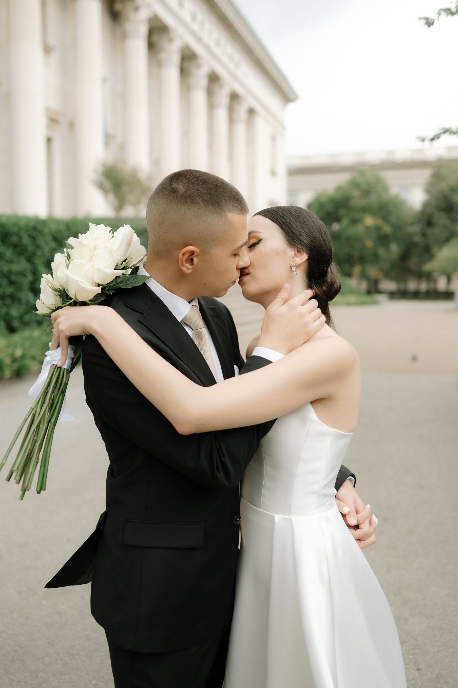 A romantic wedding moment captured in front of a columned building with white roses.