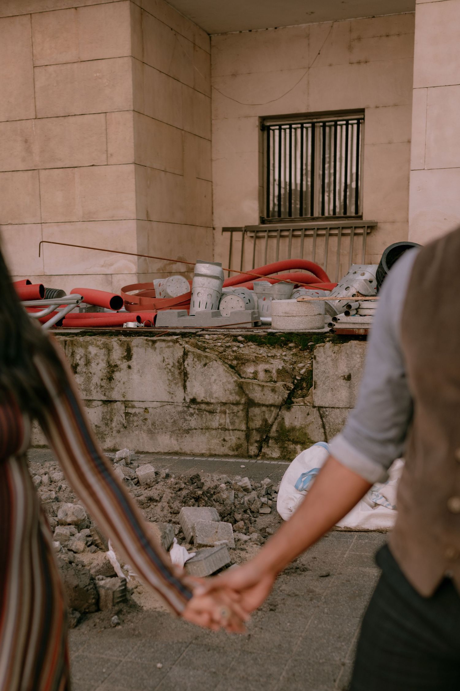 Couple holding hands in front of a construction site with debris and tools near a stone building.