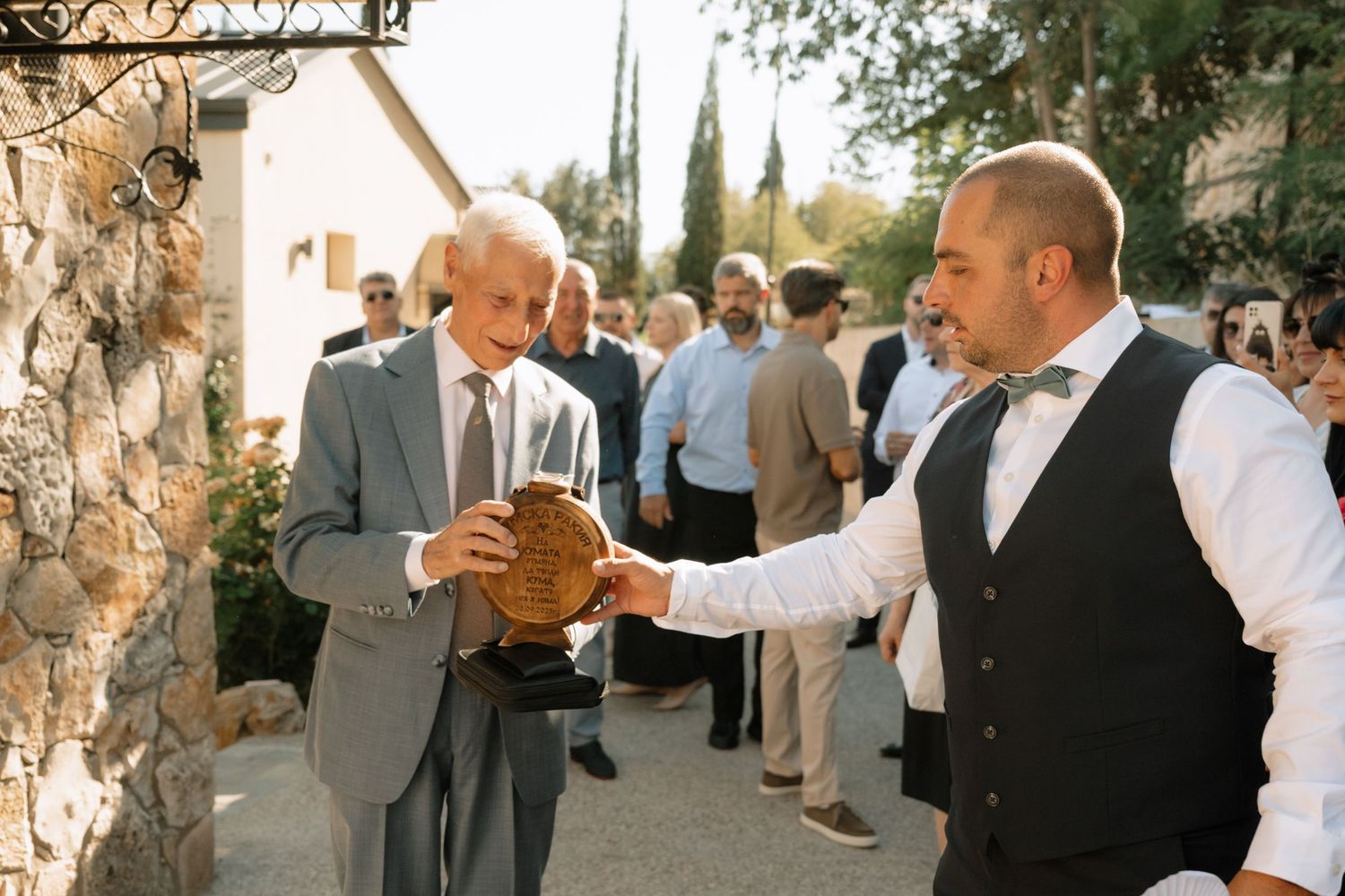 Wedding guests dance and celebrate together during an outdoor reception at a rustic venue with stone pillars.