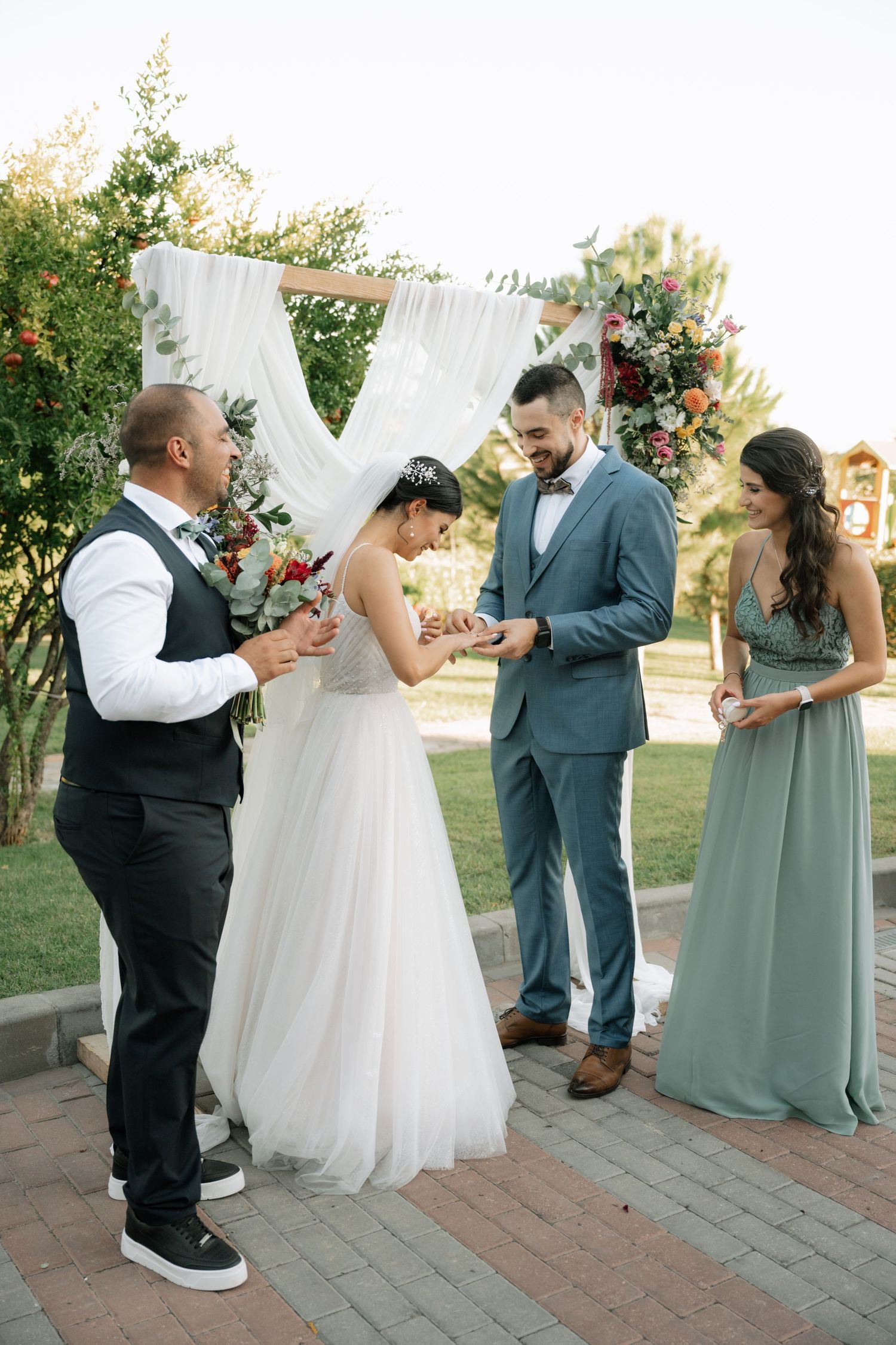 Wedding party members dance together on a brick patio during an outdoor garden reception celebration.