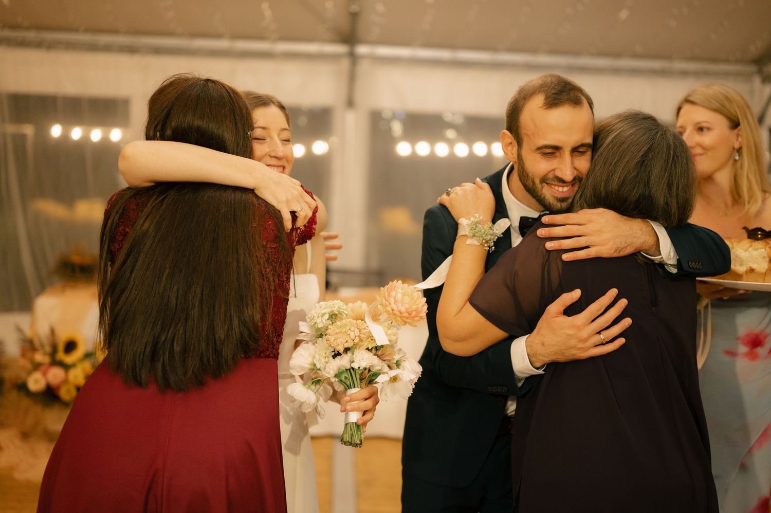 Wedding guests share warm embraces during an emotional reception moment.