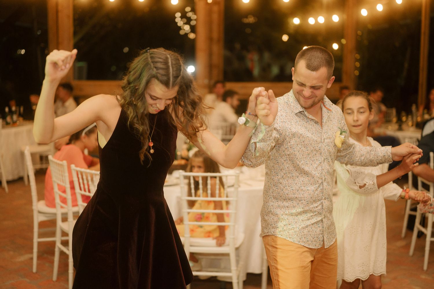 Wedding guests dance and celebrate on an outdoor dance floor under glowing string lights at night.