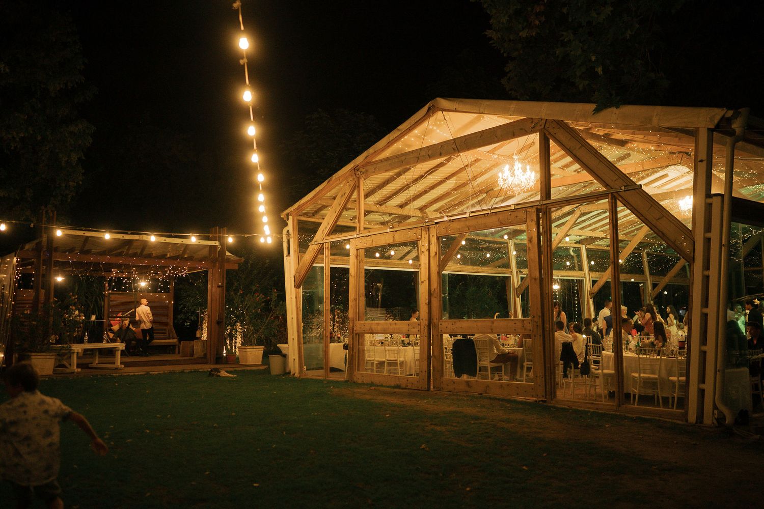 Rustic wooden pavilion illuminated by warm string lights creates an enchanting evening atmosphere at an outdoor venue.