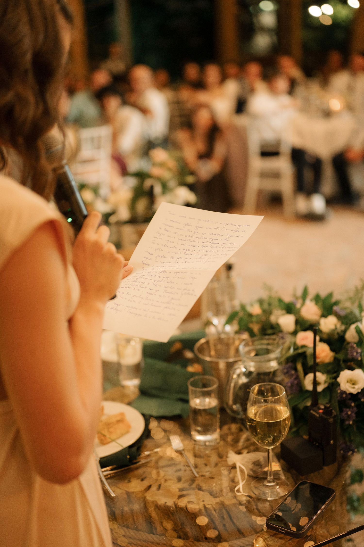 Someone reads handwritten speech or toast from paper during elegant wedding reception dinner with glowing candlelight.