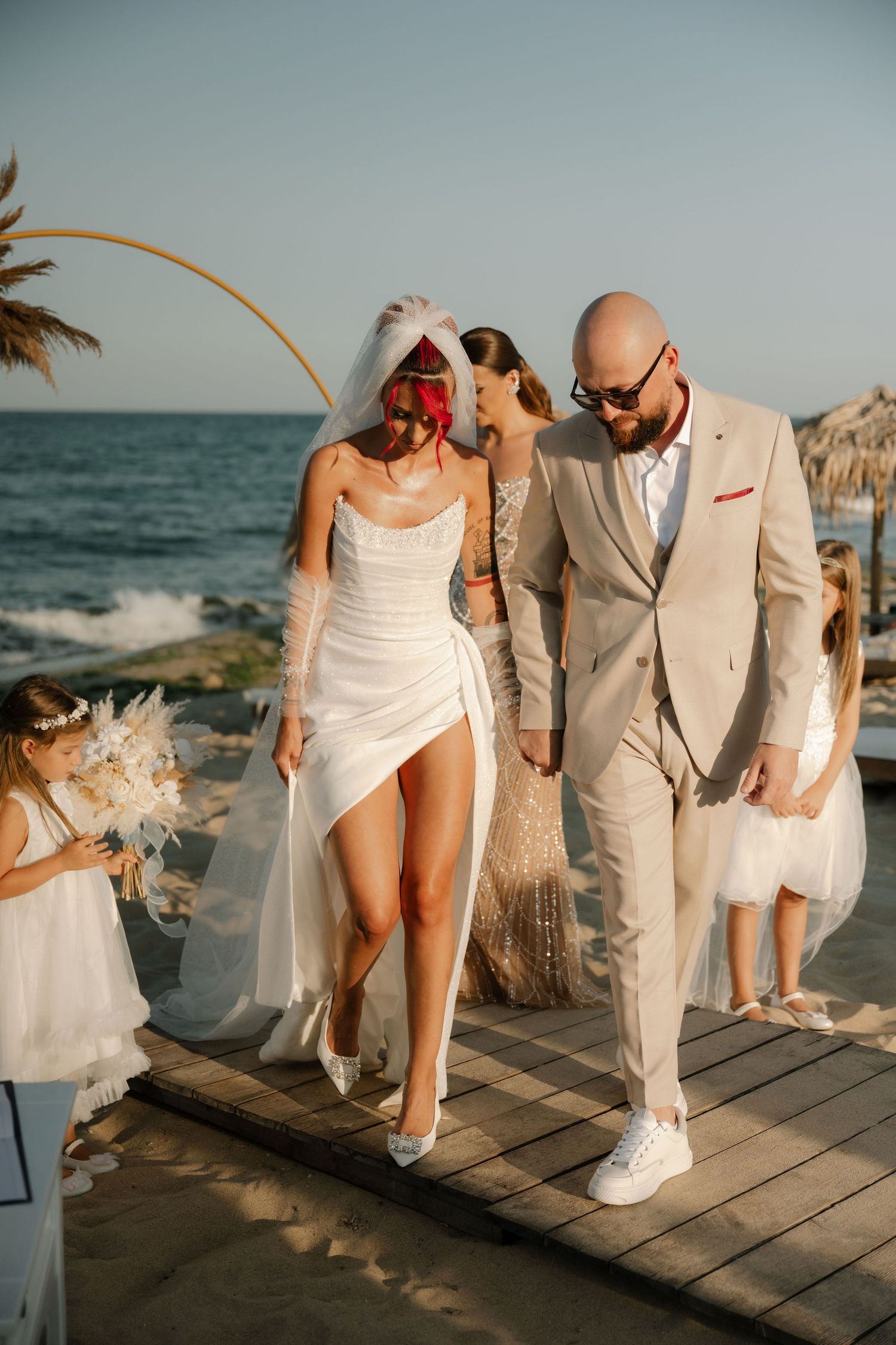 Beachside wedding celebration on wooden deck with palm trees and ocean view during golden hour.