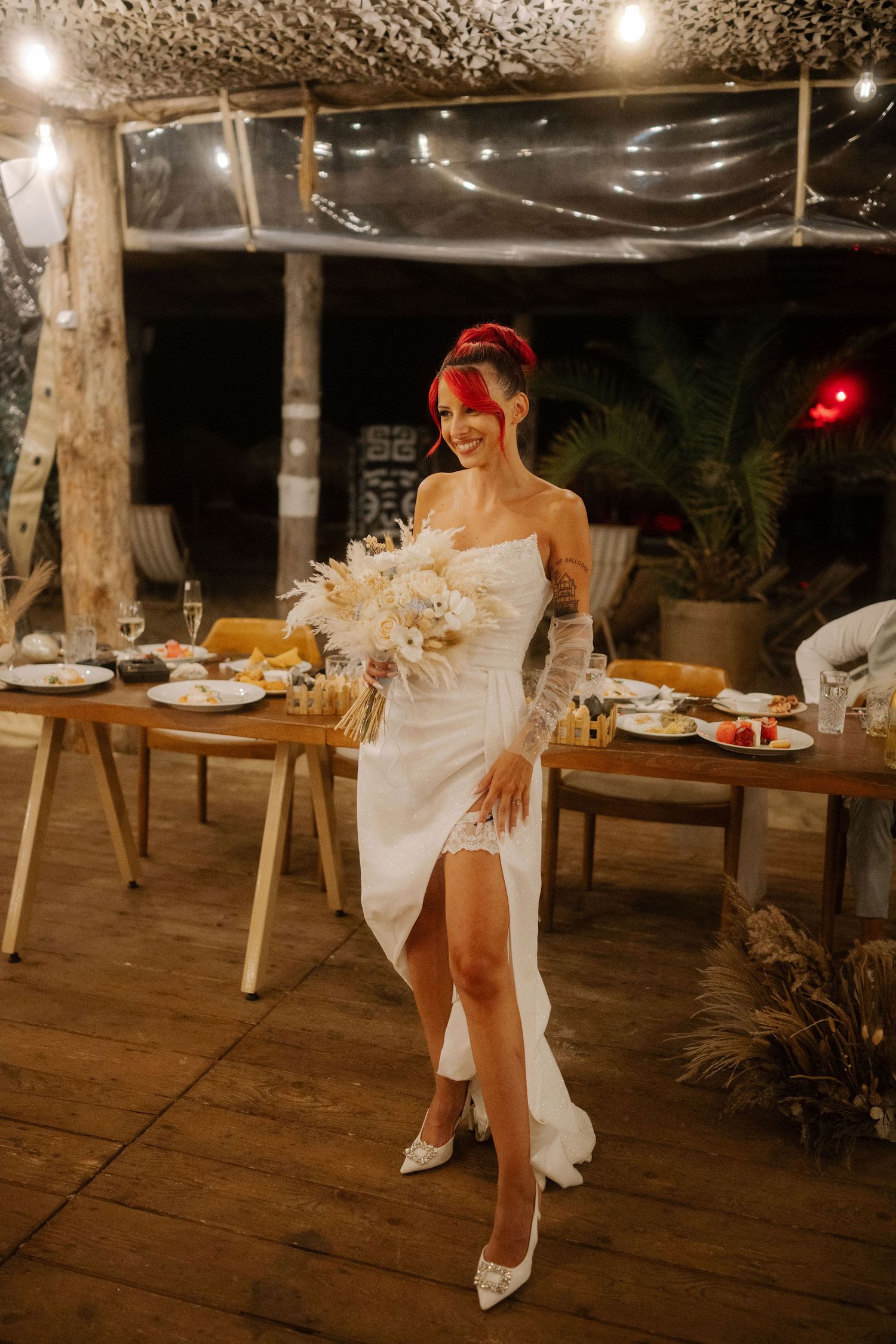 A person in a white wedding dress sits on a rustic wooden deck with string lights overhead at night.