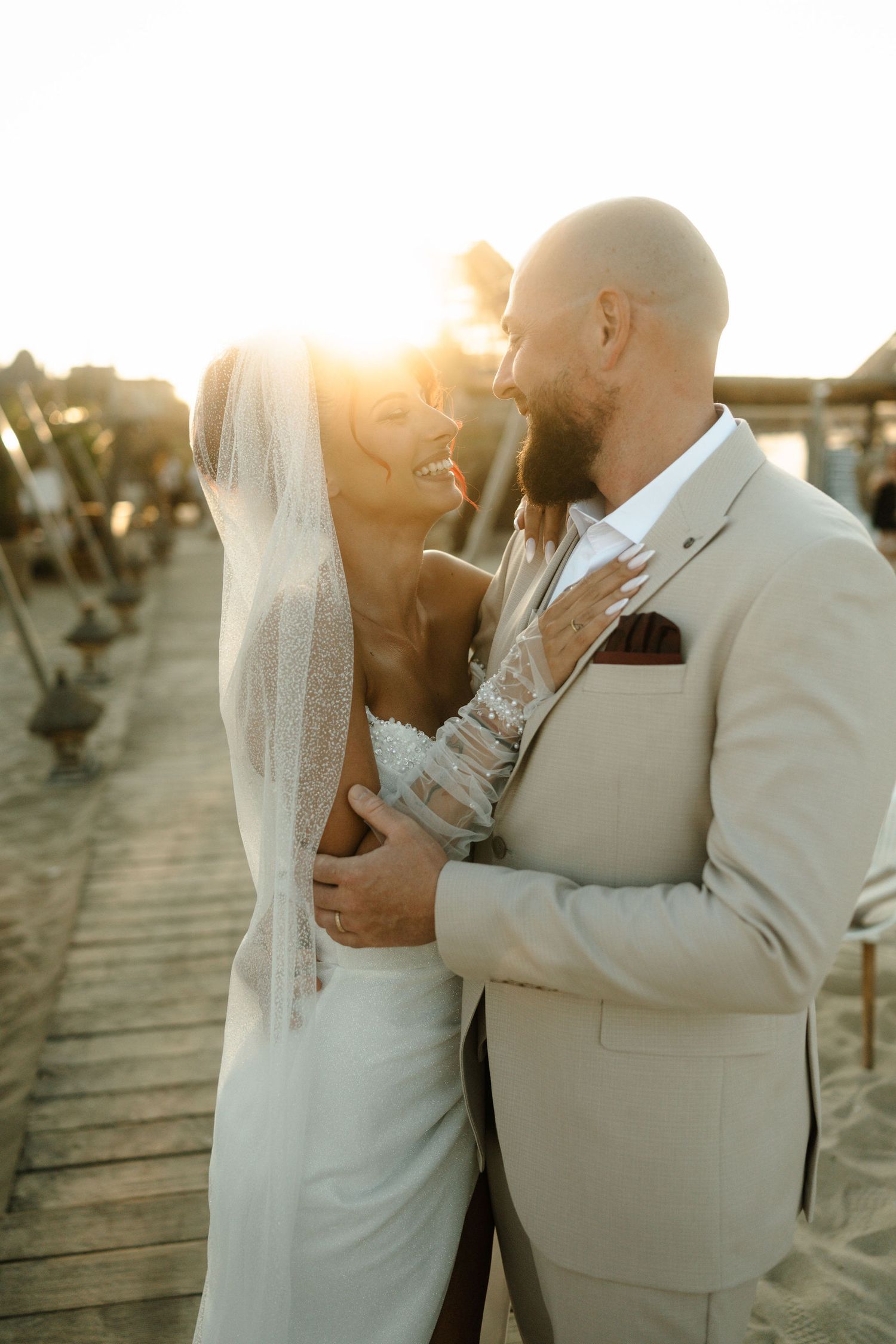 A romantic wedding couple shares intimate moments on a boardwalk during golden hour sunset.